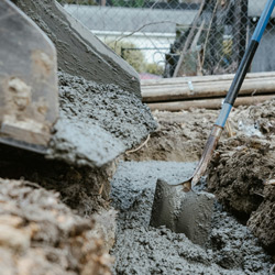 Ready mixed cement being poured into a trench with a spade being used to level the cement.